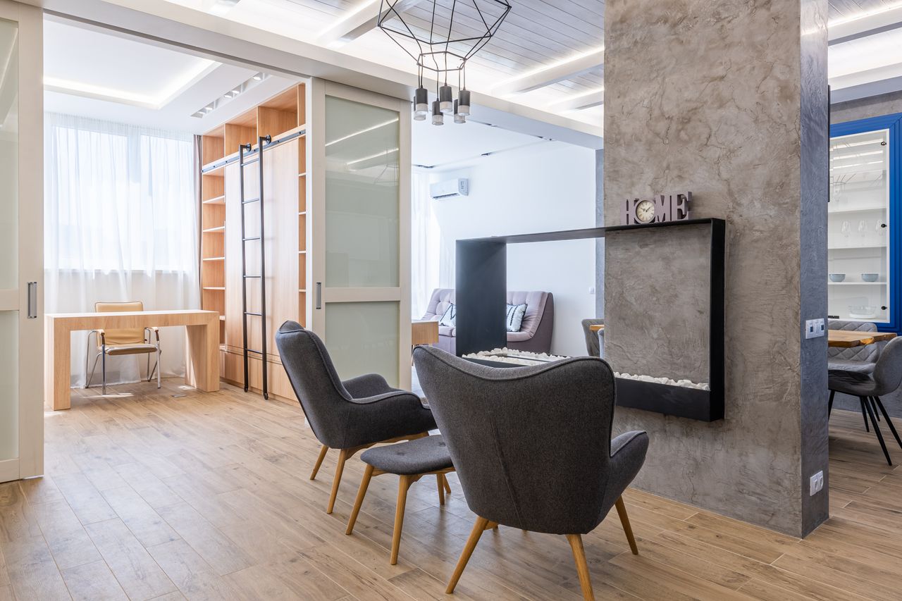 Interior of modern apartment with comfortable armchairs near glass fireplace and office zone under lights on ceiling